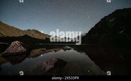 Starry sky reflected in the mountain lake Ala Kul Lake, mountain landscape by the lake at night, Ala Kul Lake, Tien Shan Mountains, Kyrgyzstan Stock Photo