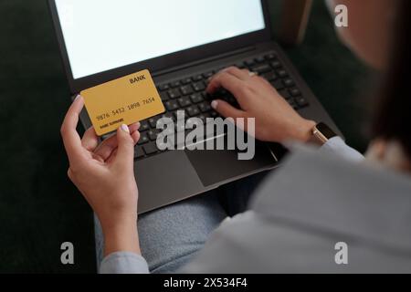 High angle of hand of young modern woman with credit card pressing keys of laptop keyboard while entering number Stock Photo