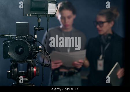 Front view closeup of professional digital video camera on stand in video production with blurred crew in background copy space Stock Photo