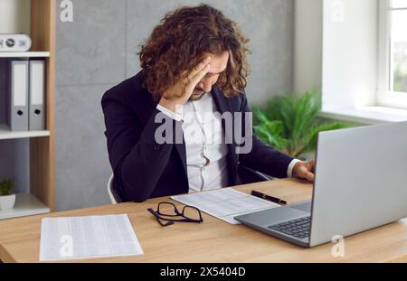 Tired business man suffering from headache working on his workplace in office. Stock Photo