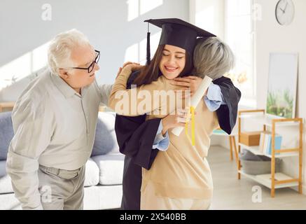 Happy graduate girl student hugging with senior parents celebrating university graduation Stock Photo