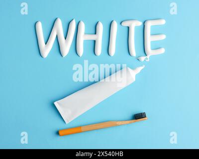 The word white written with toothpaste on blue background. Toothpaste tube and eco friendly bamboo toothbrush. Dental health, hygiene and teeth whiten Stock Photo