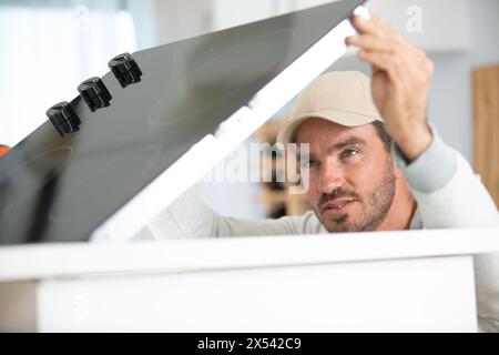 young repairman in overall repairing oven in kitchen Stock Photo