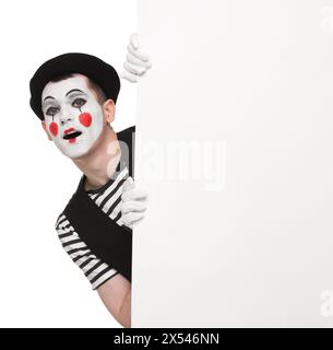 Funny mime artist peeking out of blank poster on white background Stock Photo