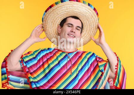 Young man in Mexican sombrero hat and poncho on yellow background Stock Photo