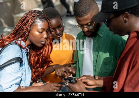Focused african american friends students looking at screen smartphone waiting results test outside. Stock Photo