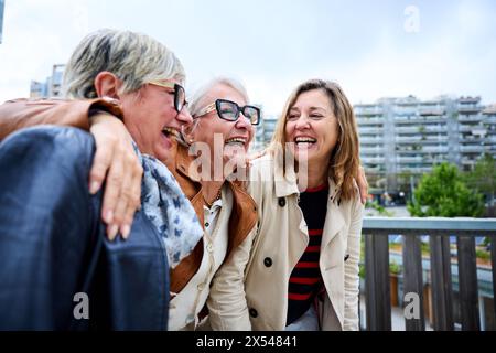 Group of three mature caucasian women enjoying embracing walk together laughing outdoor Stock Photo
