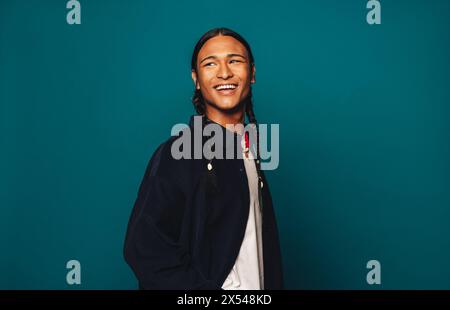 Young man with braided hair and a happy smile stands in studio with a casual and carefree look. Braided hair cascading over his shoulders, he appears Stock Photo