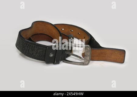 Used and Old black leather belt with buckle isolated on white background. Aged rolled-up black leather belt with a metal buckle. Stock Photo