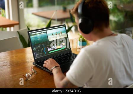 Professional video editor works on laptop with editing software, headphones on. Editing beach scene timeline, focus on creative process in home office Stock Photo