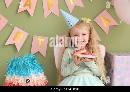 Cute little girl in party hat with donuts celebrating Birthday at home Stock Photo