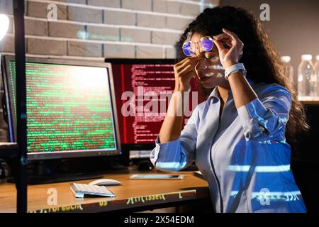 Tired female African-American programmer with eyeglasses in office at night Stock Photo