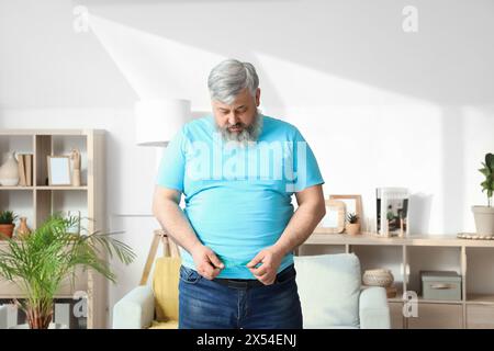 Overweight happy mature man with measuring tape at home. Weight loss concept Stock Photo