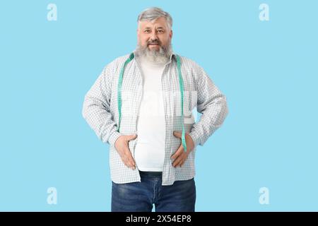Overweight happy mature man with measuring tape on blue background. Weight loss concept Stock Photo