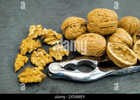 walnut (Juglans regia), Whole and cracked walnuts on a black background with nutcracker Stock Photo