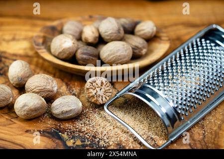 nutmeg, mace (Myristica fragrans), nutmeg on a wooden plate with a wooden spoon, whole and grated Stock Photo