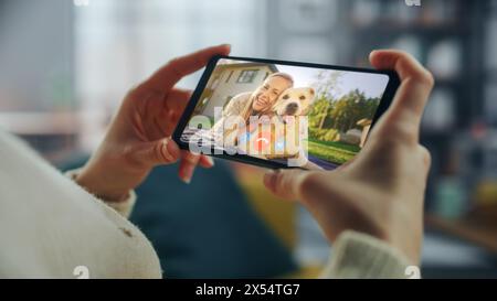 Close Up of a Female Chatting in a Video Call with Her Beautiful Friend Playing with a Dog on Smartphone from Home Living Room. Freelancer Chatting with a Client on a Call Over the Internet. Stock Photo