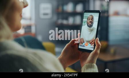Close Up of a Female Chatting in a Video Call with Her Handsome Male African American Friend on Smartphone from Home Living Room. Freelancer Making a Call with Manager Over the Internet. Stock Photo