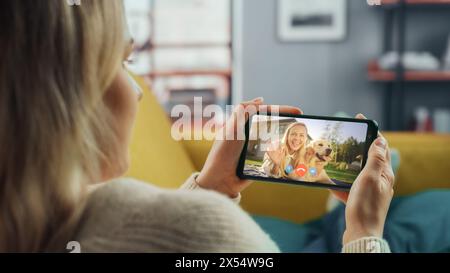 Close Up of a Female Chatting in a Video Call with Her Beautiful Friend Playing with a Dog on Smartphone from Home Living Room. Freelancer Chatting with a Client on a Call Over the Internet. Stock Photo