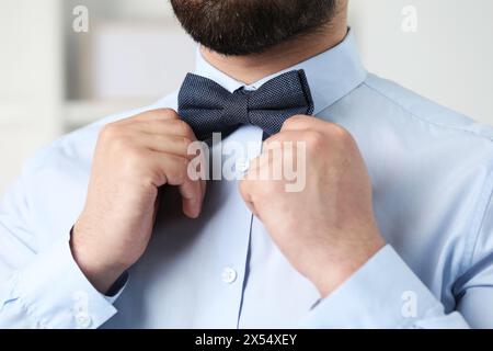 Man in shirt adjusting bow tie indoors, closeup Stock Photo