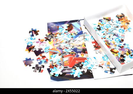 On a white background lies a cardboard box from which multi-colored puzzles have fallen. Stock Photo