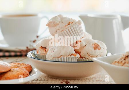 closeup of some merengues almendrados, spanish baked meringues with almonds, in a ceramic plate placed on a set table next to a cup of coffee Stock Photo