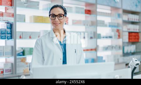 Pharmacy Counter: Portrait of Beautiful Professional Caucasian Female Pharmacist Working on Computer, Looks at Camera Smiling Charmingly. Drugstore Store with Shelves Health Care Products Stock Photo
