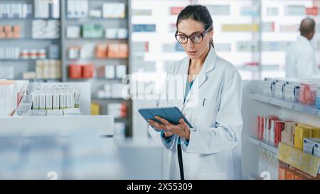 Pharmacy Drugstore: Beautiful Caucasian Pharmacist Uses Digital Tablet Computer, Checks Inventory of Medicine, Drugs, Vitamins, Health Care Products on a Shelf. Professional Pharmacist in Pharma Store Stock Photo