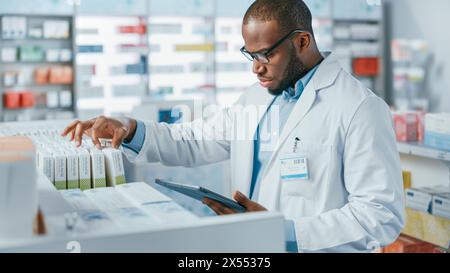 Pharmacy: Portrait of Professional Black Pharmacist Uses Digital Tablet Computer, Checks Inventory of Medicine, Drugs, Vitamins, Health Care Products on a Shelf. Pharmacist in Drugstore Store Stock Photo