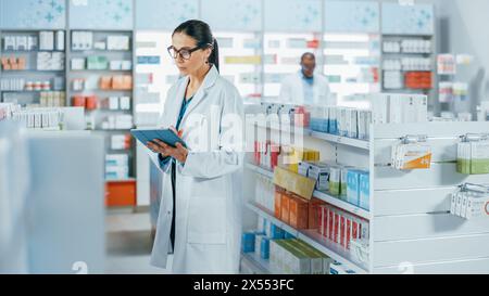 Pharmacy Drugstore: Beautiful Caucasian Pharmacist Uses Digital Tablet Computer, Checks Inventory of Medicine, Drugs, Vitamins, Health Care Products on a Shelf. Professional Pharmacist in Pharma Store Stock Photo