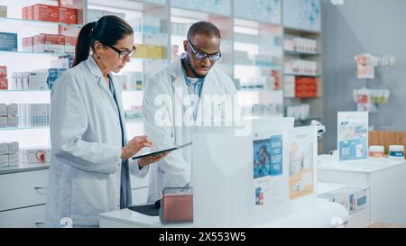 Pharmacy Behind the Checkout Counter: Black Male and Caucasian Female Pharmacists Talk about Medicine, Use Digital Tablet Computer. Medical Professionals in Drugstore with Health Care Products Stock Photo