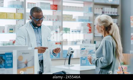 Pharmacy Drugstore Checkout Counter: Black Male Pharmacist Explains Use and Manual for Prescription Medicine Beautiful, Senior Female Customer Paying Using Contactless Credit Card to Terminal Stock Photo