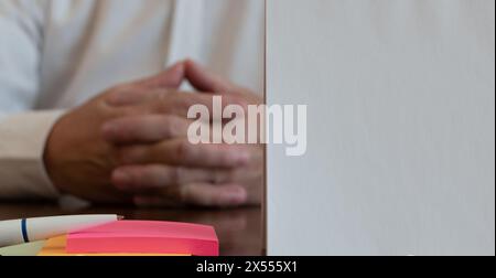 White sheet of paper and ballpoint pen on multi-colored paper stickers close-up on blurred background of forefinger of middle-aged man Stock Photo