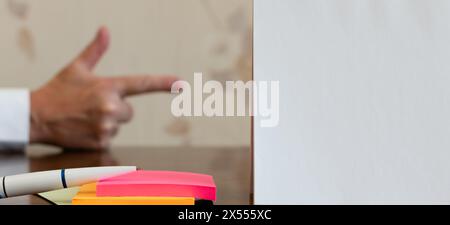 White sheet of paper and ballpoint pen on multi-colored paper stickers close-up on blurred background of forefinger of middle-aged man Stock Photo