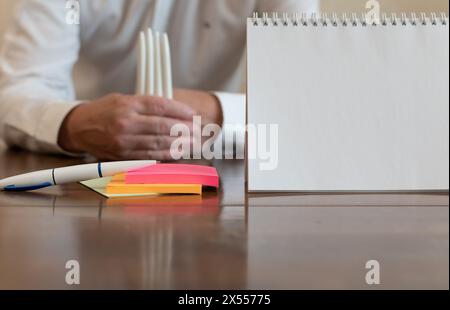 White sheet of paper and ballpoint pen on multi-colored paper stickers close-up on blurred background of forefinger of middle-aged man Stock Photo
