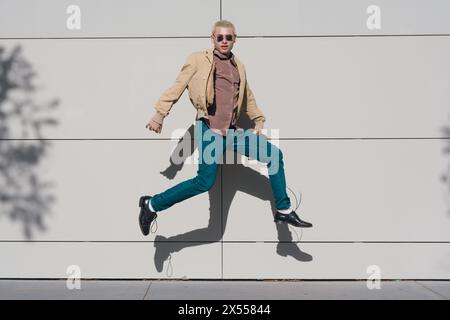 A young latin man in a tan jacket and blue jeans is jumping in the air in a sunny day. The image has a lighthearted and playful mood, as the man is ha Stock Photo