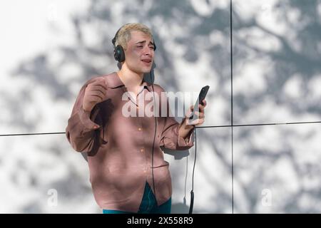 A young latin man in a brown shirt is holding a cell phone and headphones. He is listening to music and he is enjoying himself at sunset. Stock Photo