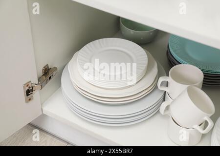 Clean plates and cups on shelf in cabinet indoors Stock Photo