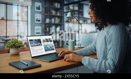 Back View Shot of a Young Female Using Laptop Computer, Reading Latest News for Market Analysis. Freelancer Female at Home Living Room while Sitting at a Table and Using Computer. Stock Photo