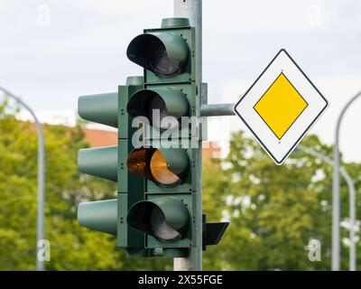 Traffic light blinking yellow and priority road sign next to it. The light signal is broken of switched off. The car drivers must look at the signs. Stock Photo
