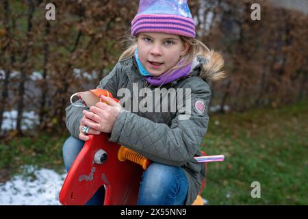 Girls love horses. When there is no animal around, children like to play in a playground where there is a red rocking horse. Healthy in cold weather. Stock Photo