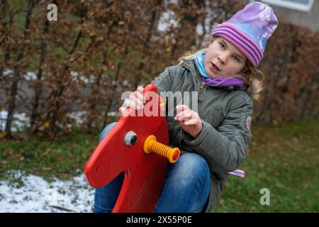 Girls love horses. When there is no animal around, children like to play in a playground where there is a red rocking horse. Healthy in cold weather. Stock Photo