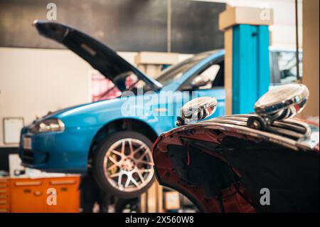 Lifted car with opened bonnet and with reflection on window glass while in repair workshop of garage equipped with various instruments for service and Stock Photo