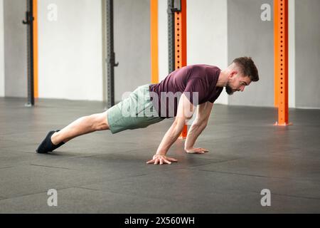 Full body side view of strong bearded adult male in sportswear looking down while lying on gym floor doing calisthenics plank lean exercise in dayligh Stock Photo
