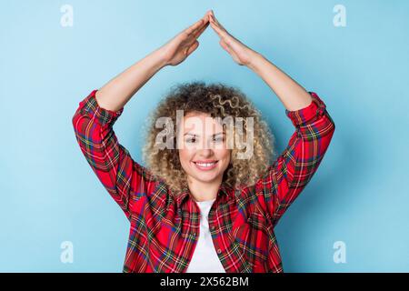 Photo of positive reliable lady show roof form raise hands wear checkered shirt isolated blue color background Stock Photo