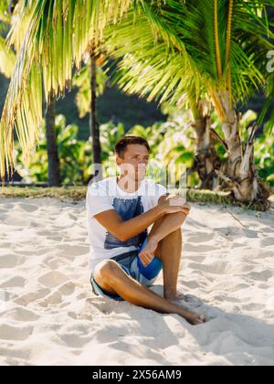 Handsome guy relaxing and sitting on the beach. Slim man vacation on paradise beach Stock Photo