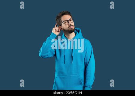 Thoughtful Young Man in Glasses, Blue Hoodie Against Plain Background Stock Photo