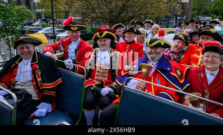 Town criers smile (bellmen & bellwomen in colourful braided crier's livery uniforms) sitting on open-top bus deck - Ilkley, West Yorkshire England UK. Stock Photo