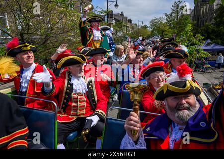 Town criers smile (bellmen & bellwomen in colourful braided crier's livery uniforms) sitting on open-top bus deck - Ilkley, West Yorkshire England UK. Stock Photo