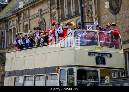 Town criers smile (bellmen & bellwomen in colourful braided crier's livery uniforms) standing on open-top deck - Ilkley, West Yorkshire England UK. Stock Photo